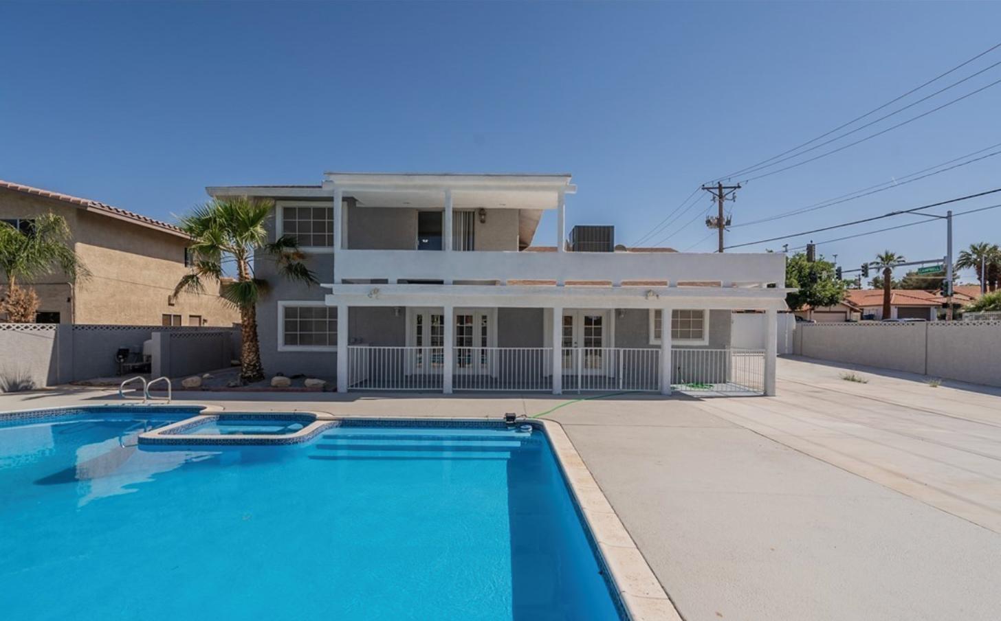 A gray home featuring a large, partially covered balcony, covered patio, massive outdoor space with a large pool and a palm tree